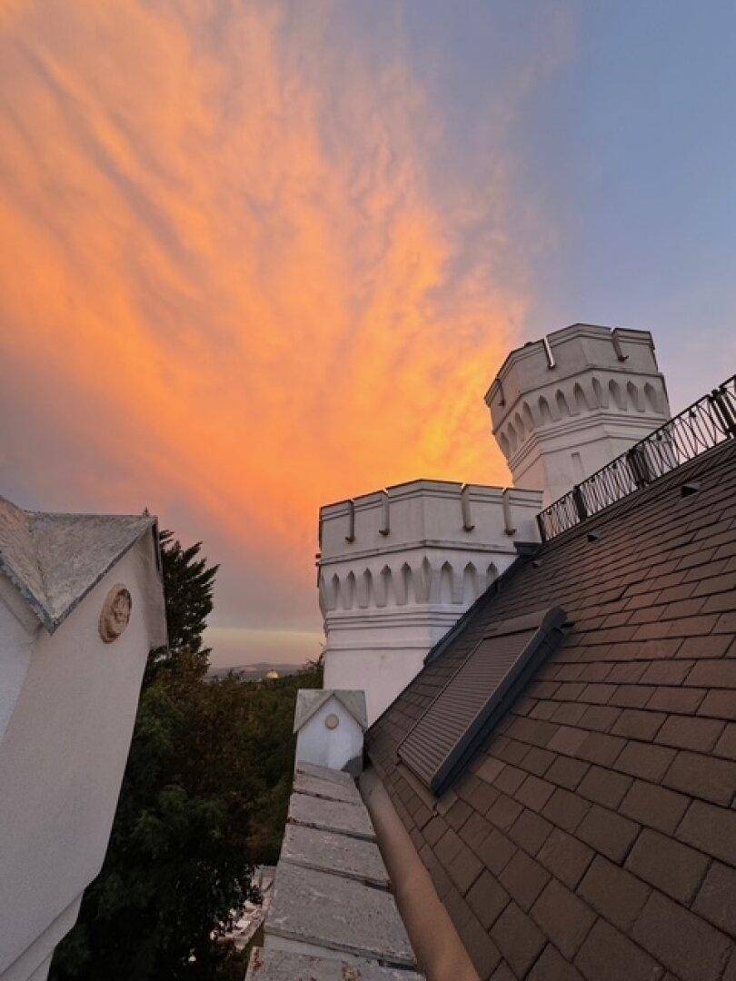 Dächer und Türme der Villa bei einem spektakulären Sonnenuntergang mit leuchtend orangefarbenem Himmel.