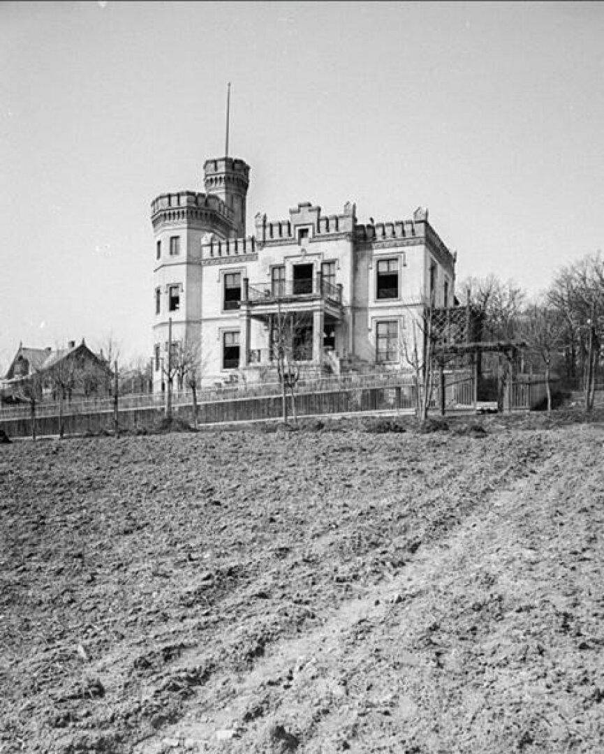 Historisches Schwarz-Weiß-Foto der Villa, umgeben von einem Feld, das ihre ursprüngliche ländliche Lage zeigt.