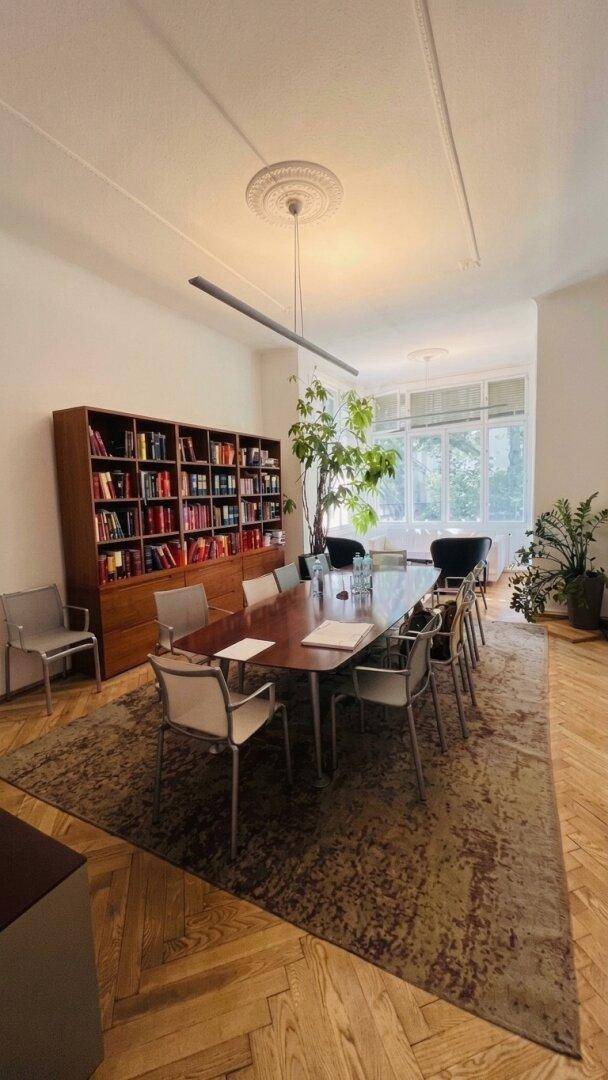 Geräumiger Büroraum mit großem Konferenztisch, Bücherregal und Fischgrätparkett.