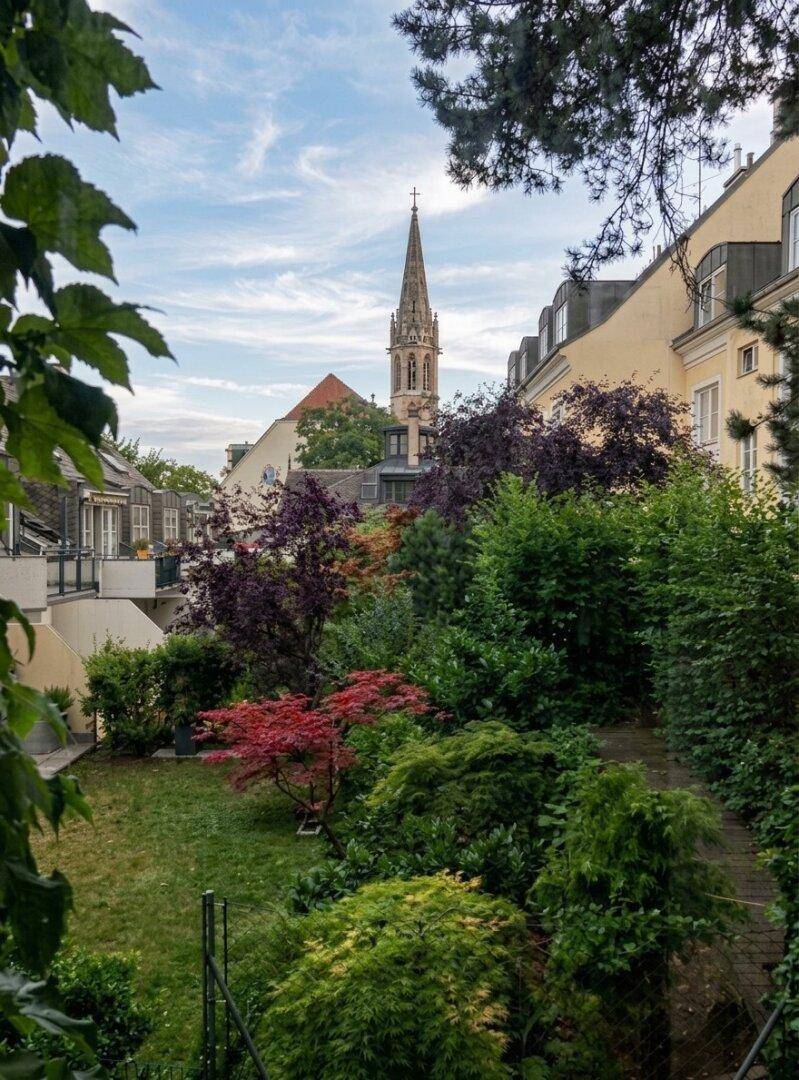 Üppiger Garten mit vielfältiger Bepflanzung und Blick auf eine Kirchturmspitze.