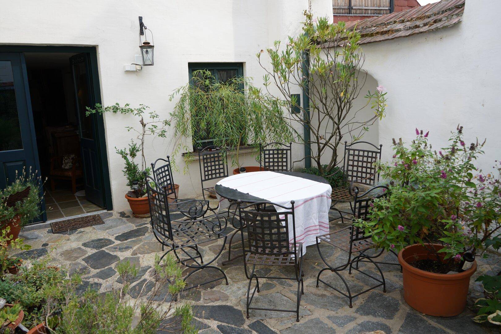 Gemütlicher Innenhof mit schmiedeeisernen Gartenmöbeln und vielen blühenden Pflanzen.