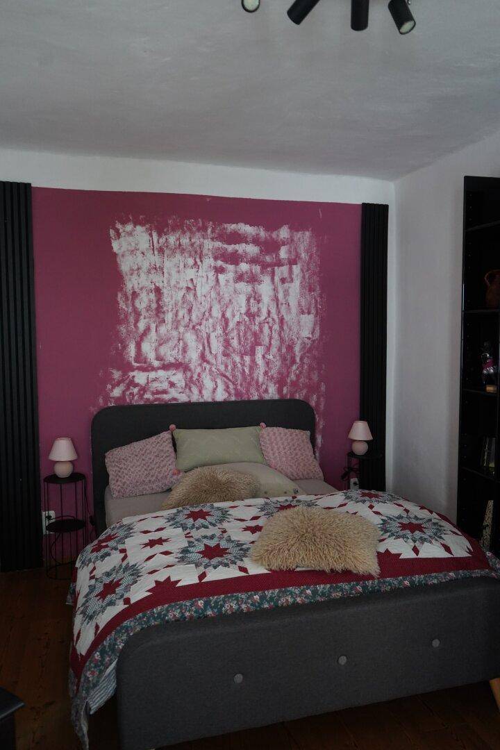 Schlafzimmer mit einer auffälligen pinkfarbenen Wand, einem Doppelbett und Holzdielenboden.