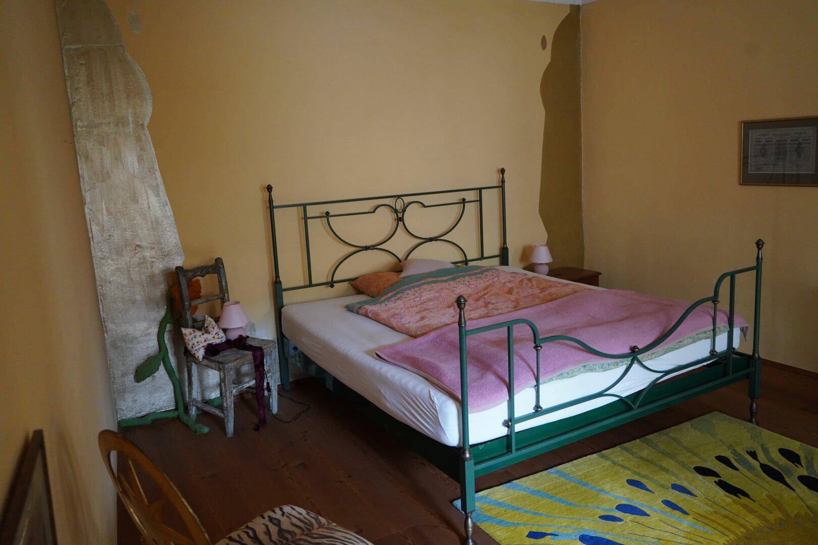 Schlafzimmer mit gelben Wänden, einem schmiedeeisernen Bett und Holzdielenboden.