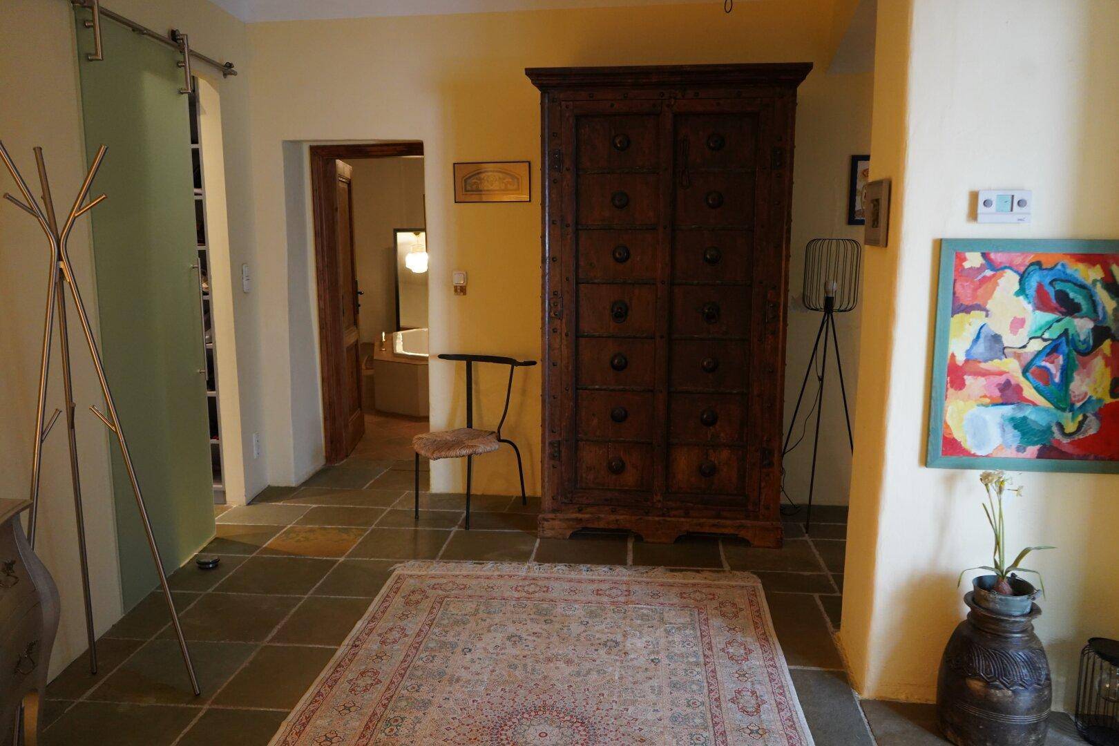 Flur mit einem großen Holzschrank, Kunstwerken und einem Teppich auf gefliestem Boden.