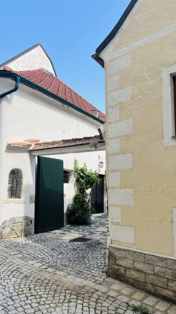 Schmale Gasse mit Kopfsteinpflaster zwischen historischen Gebäuden und einem grünen Holztor.