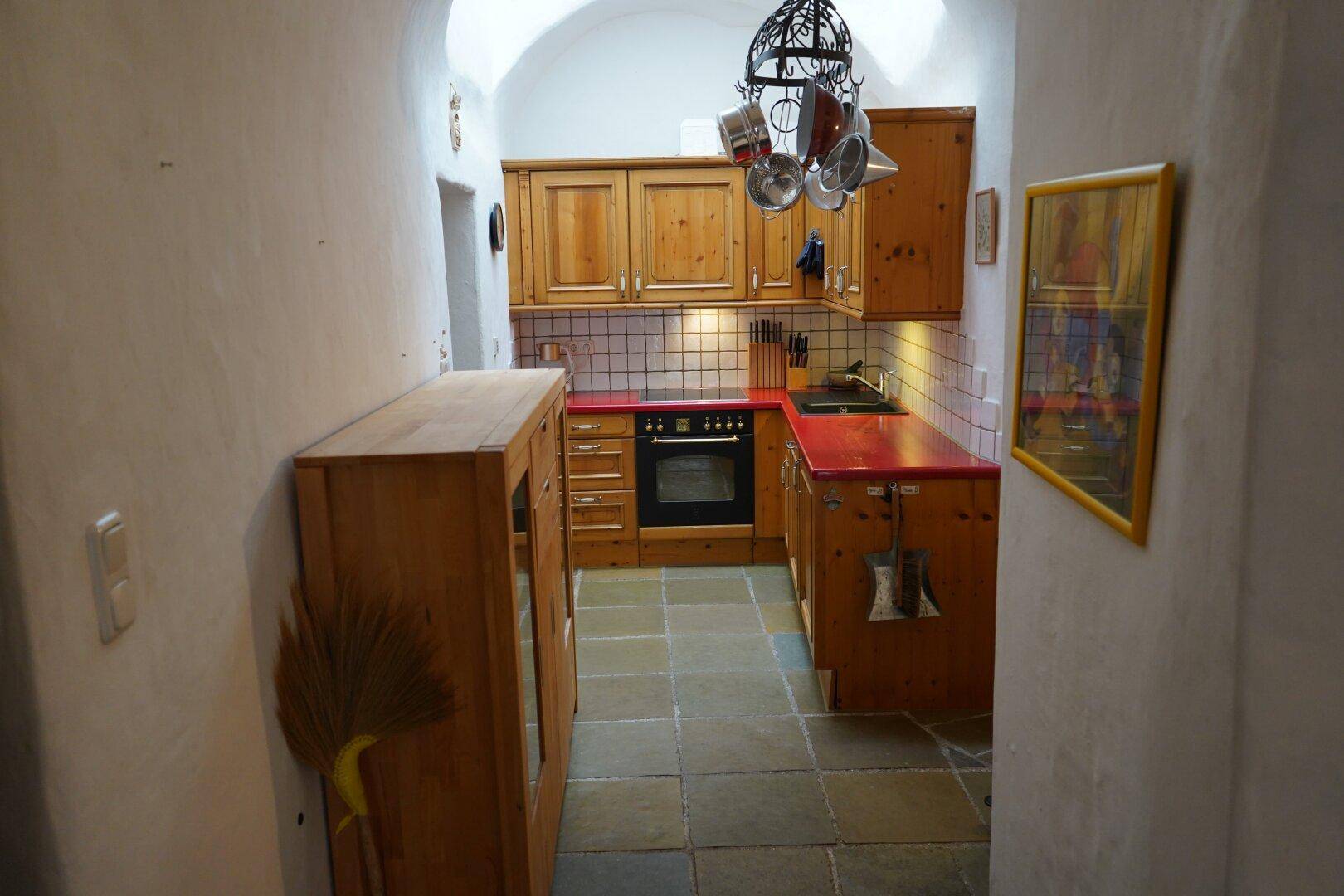 Schmale Küche mit Holzschränken, roten Arbeitsplatten und Steinbodenfliesen.