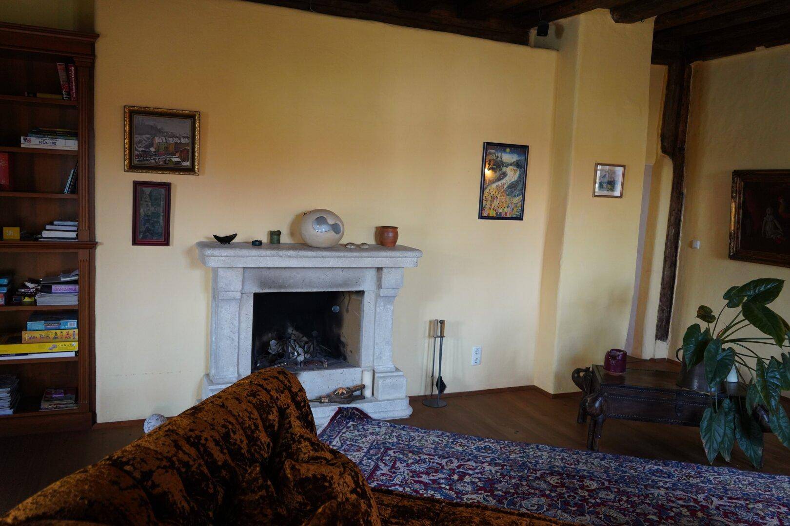 Wohnzimmer mit rustikalem Steinkamin, bequemer Couch und sichtbaren Holzbalken an der Decke.