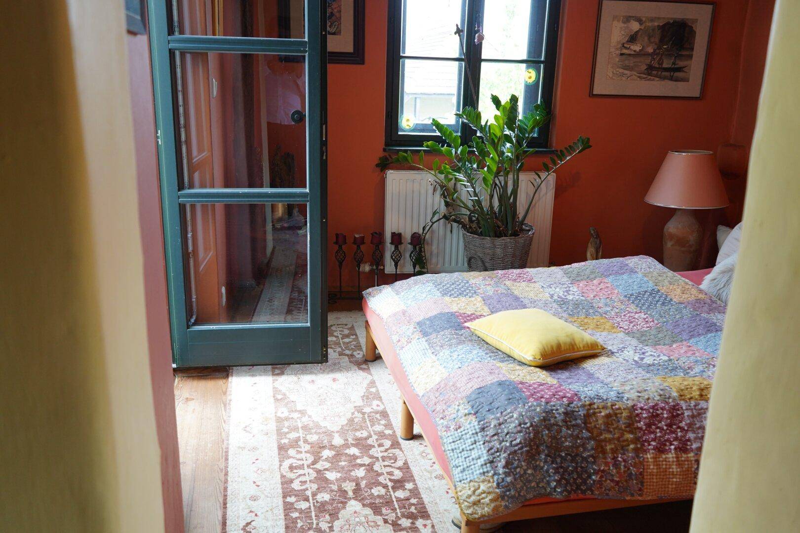 Schlafzimmer mit orangefarbenen Wänden, einem Fenster und einer Tür, die zu einem anderen Raum führt.