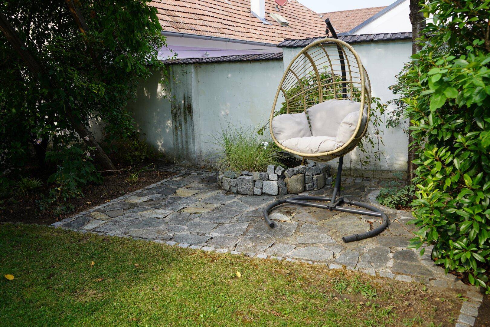 Gartenbereich mit gepflasterter Terrasse, einem Hängesessel und einer kleinen Steingartenanlage.