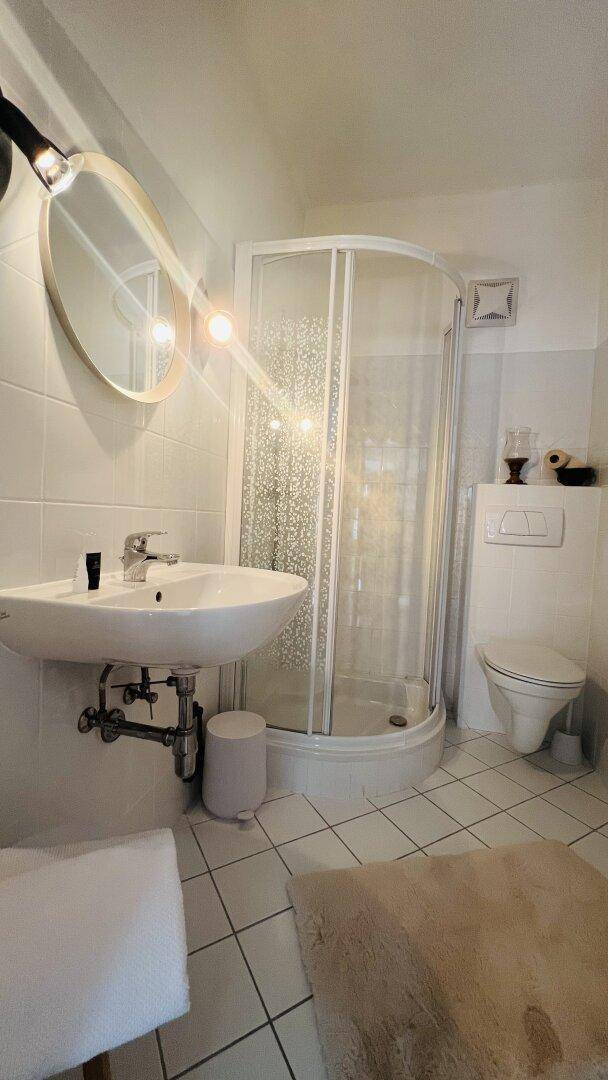 Modernes Badezimmer mit Duschkabine, Waschbecken und Toilette, hell gefliest.
