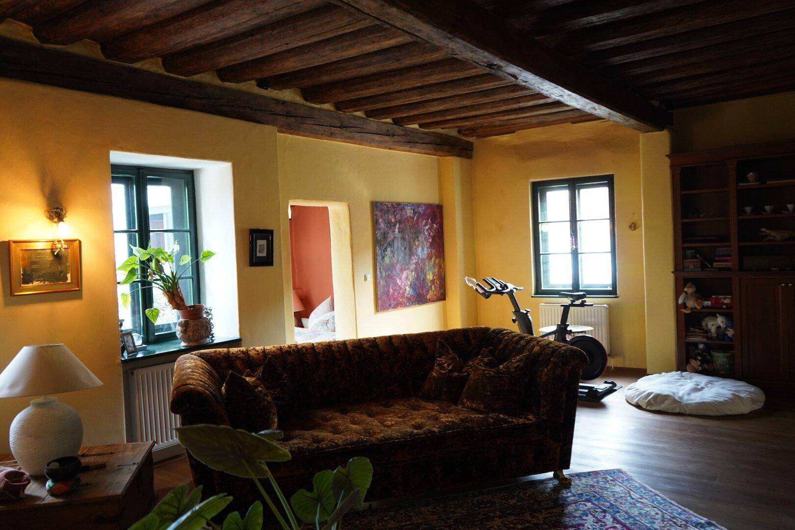 Geräumiges Wohnzimmer mit großem Sofa, Holzboden und charakteristischen Holzbalken an der Decke.