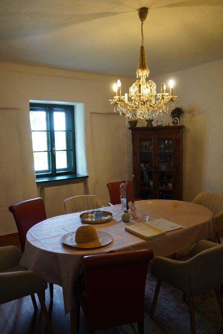 Gemütliches Esszimmer mit ovalem Tisch, Kronleuchter und einem Fenster mit Blick nach draußen.