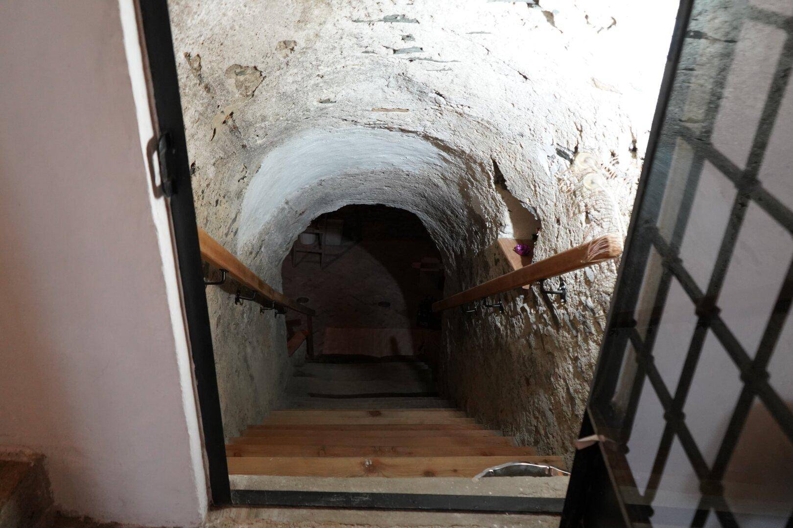 Dunkle, schmale Steintreppe führt hinab in einen historischen Kellerraum.