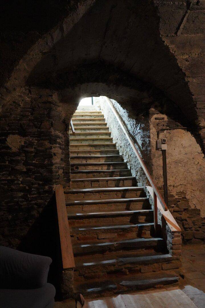 Historische Steintreppe führt aus einem dunklen Kellerraum nach oben ins Licht.