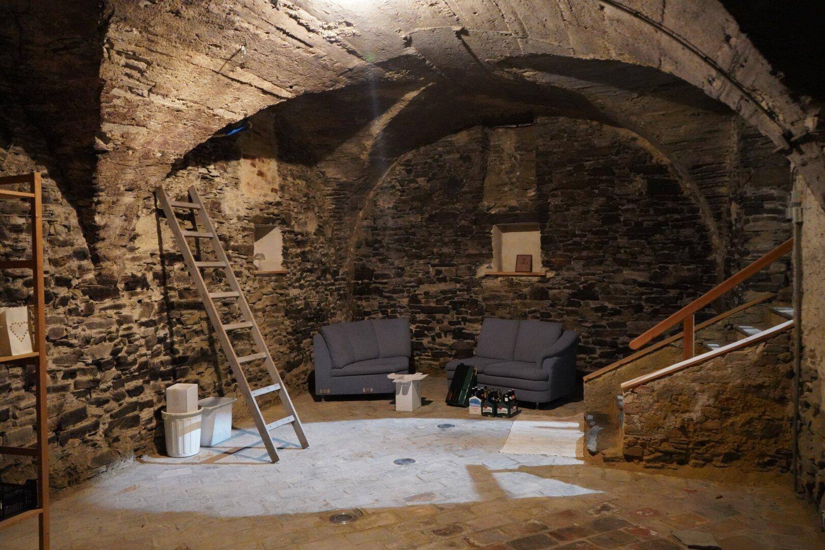 Gemütlicher Gewölbekeller mit Steinmauern, Sitzgelegenheiten und Flaschenlagerung, ideal für gesellige Abende.