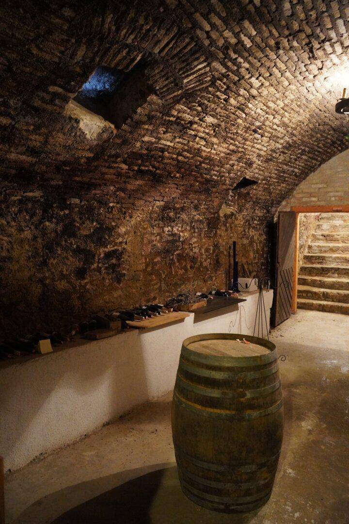 Historischer Weinkeller mit gewölbter Ziegeldecke, Weinregalen und einem Holzfass.