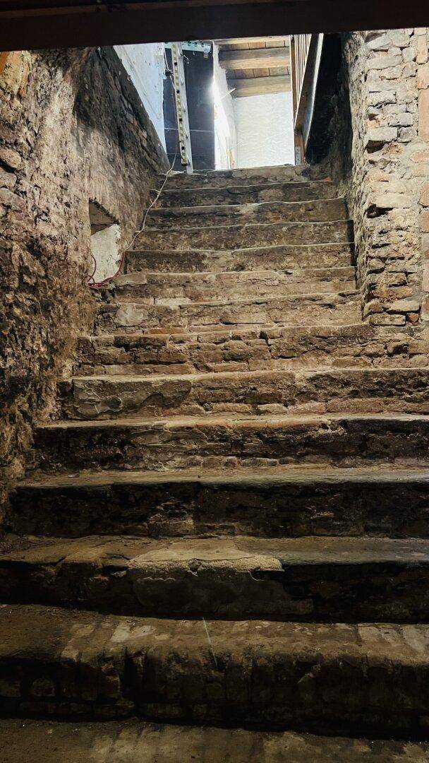 Rustikale Steintreppe in einem alten Keller, umgeben von grobem Mauerwerk.