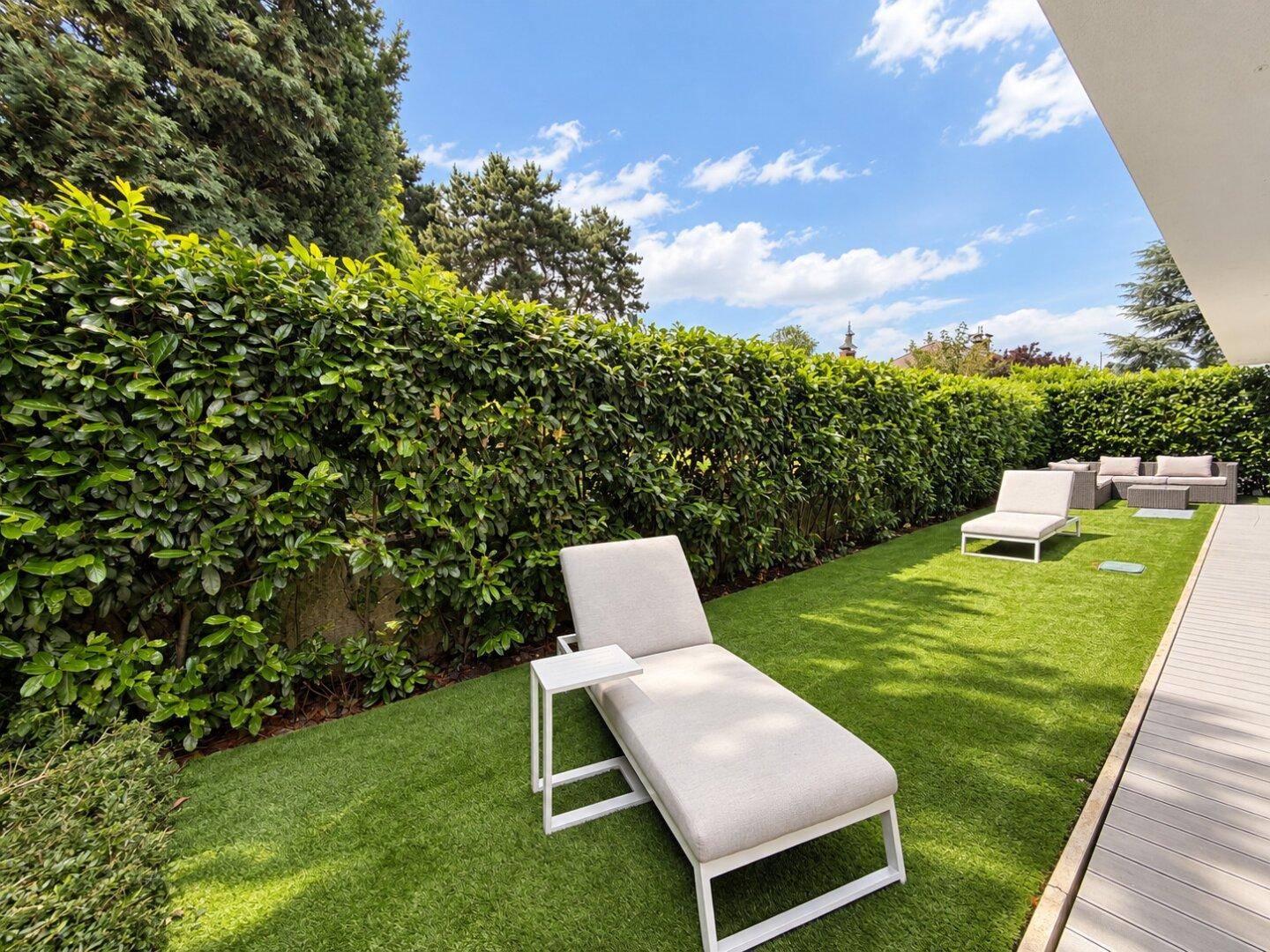 Sonniger Gartenbereich mit Liegestühlen und hoher Hecke für Privatsphäre.