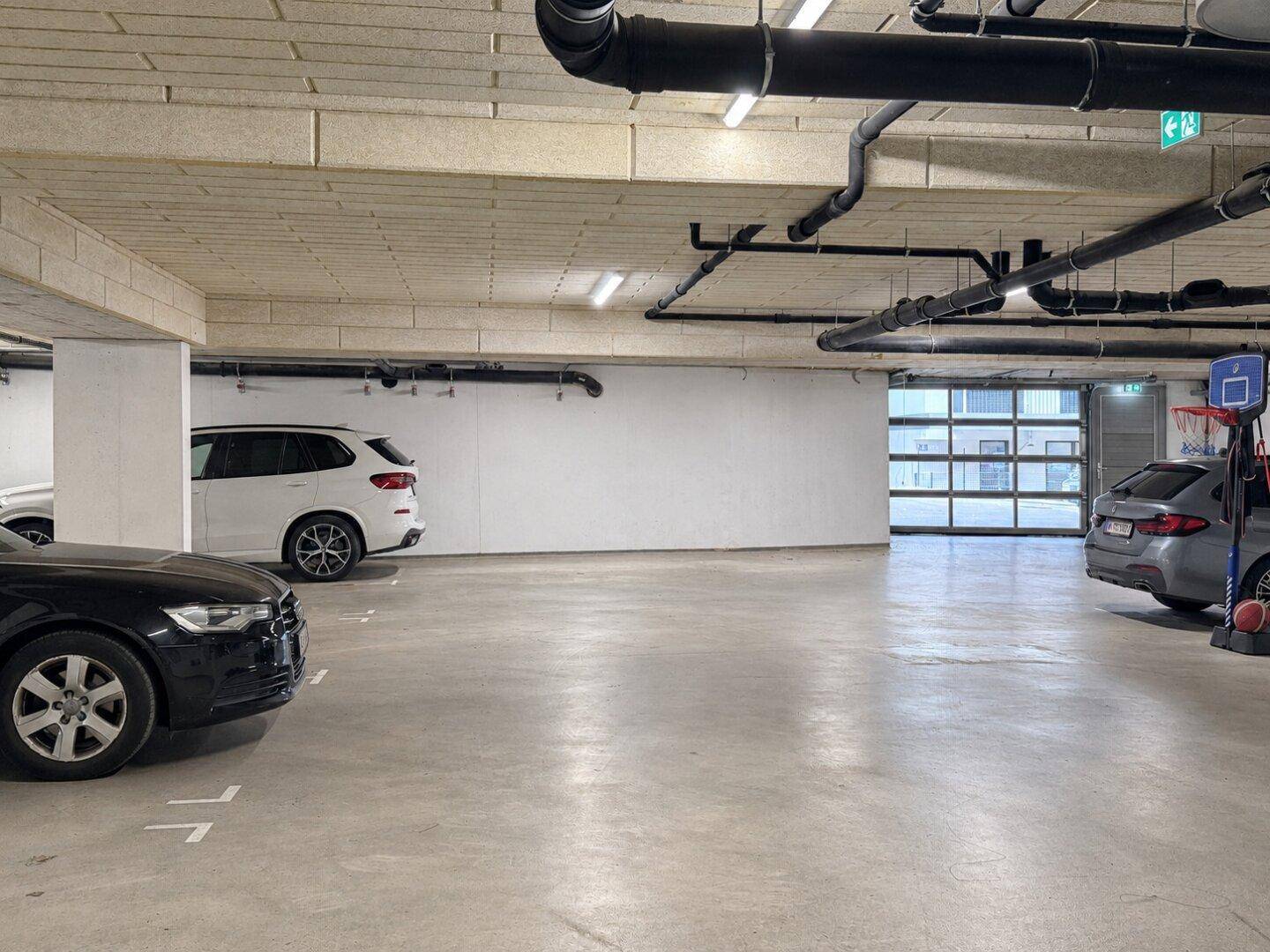 Helle Tiefgarage mit mehreren Stellplätzen und Zugangstor.