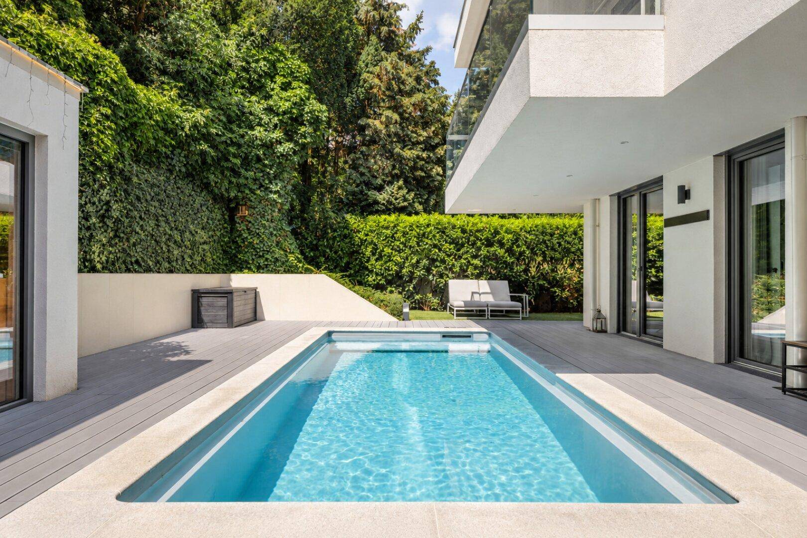 Elegante Terrasse mit privatem Pool und Liegefläche, umgeben von Grün.