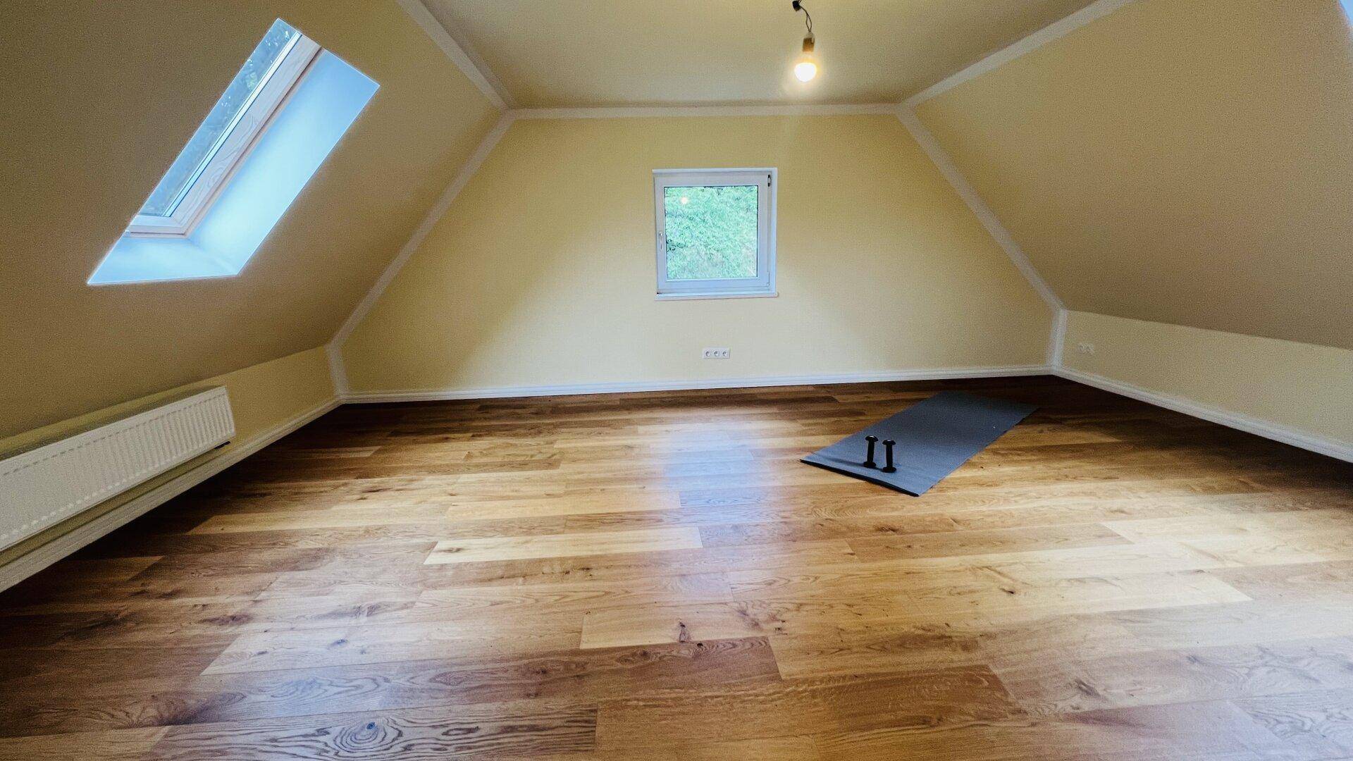 Geräumiges Dachzimmer mit Holzboden, Dachschräge und einem großen Dachfenster für viel Licht.
