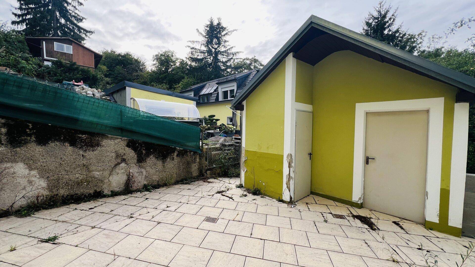 Gepflasterter Außenbereich mit einem kleinen Nebengebäude und Blick ins Grüne.