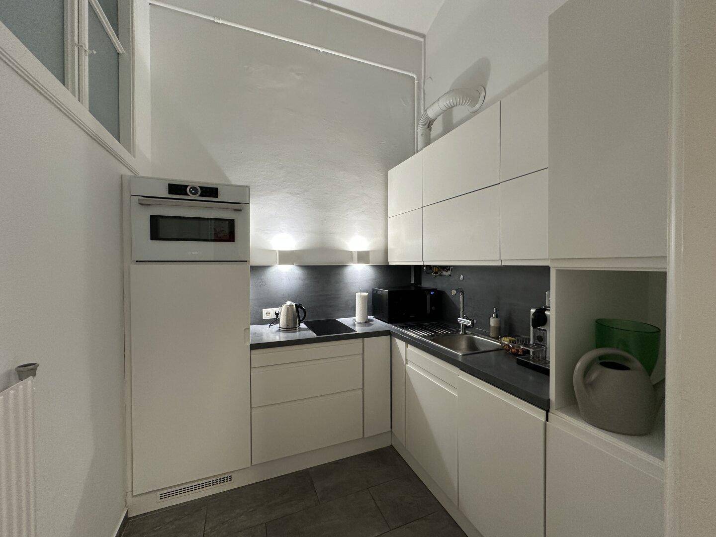 Moderne, kompakte Küche mit weißen Schränken, integriertem Backofen und Fliesenboden.