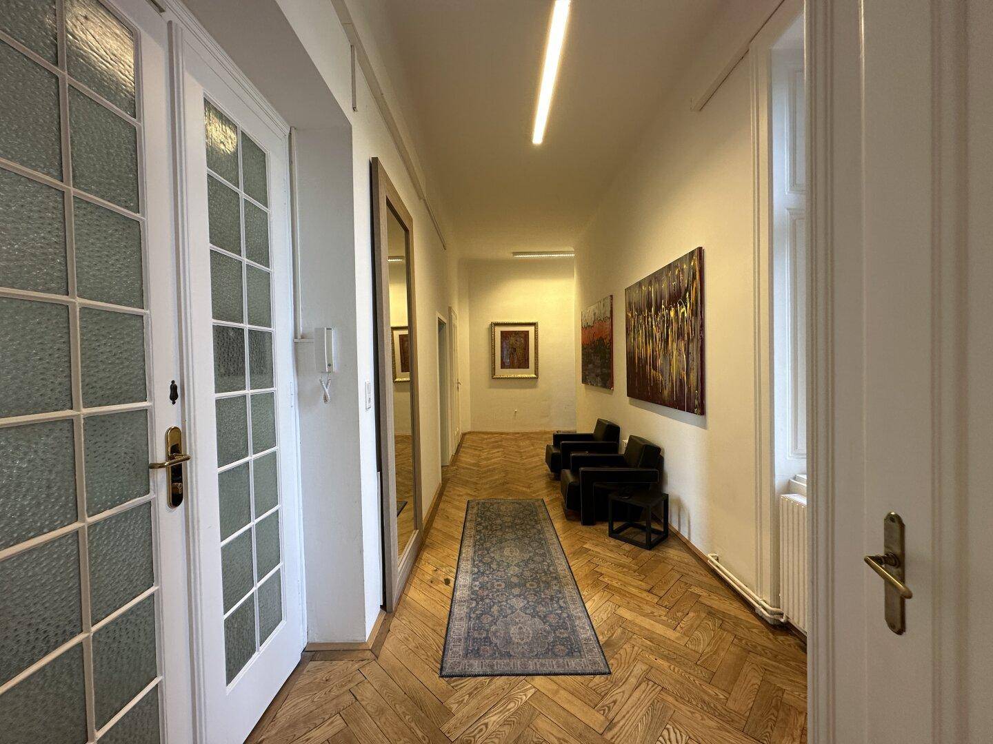 Heller Flur mit Fischgrätparkett, modernen Kunstwerken und Spiegeltüren.