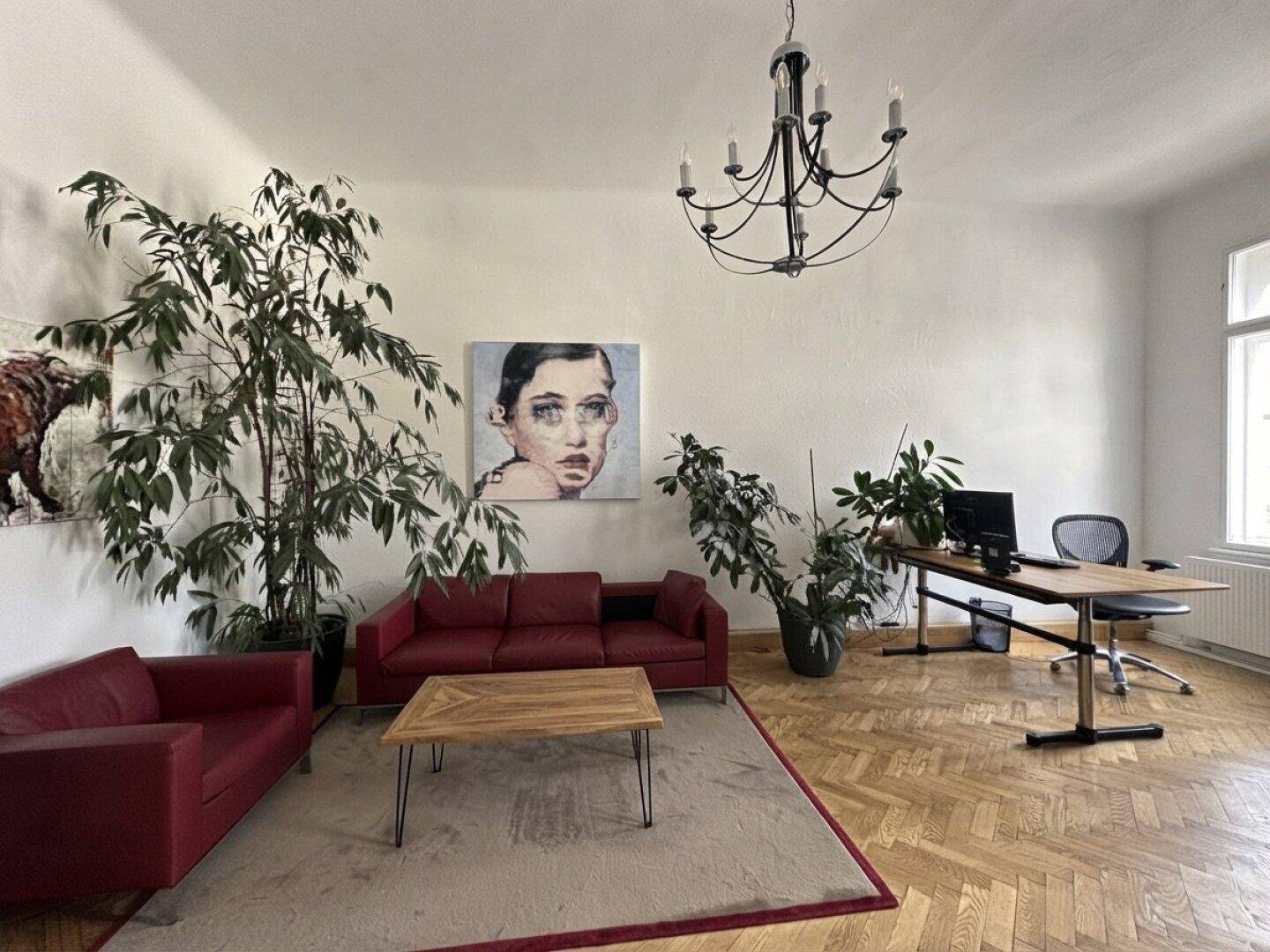 Großzügiges Büro mit Fischgrätparkett, roten Sofas und viel Tageslicht.