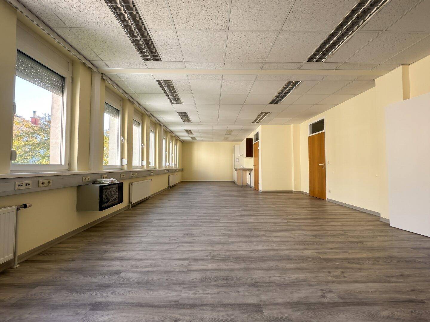 Leeres Großraumbüro mit vielen Fenstern, abgehängter Decke und modernem Laminatboden, bereit zur Einrichtung.