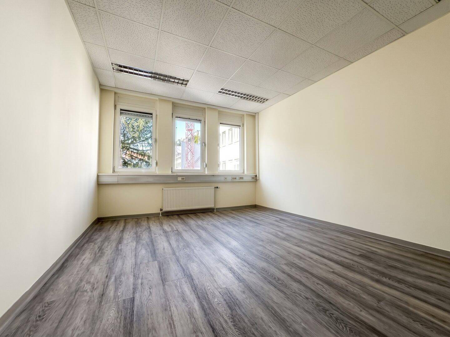 Leeres Einzelbüro mit Laminatboden und großen Fenstern, ideal für individuelle Arbeitsbereiche.