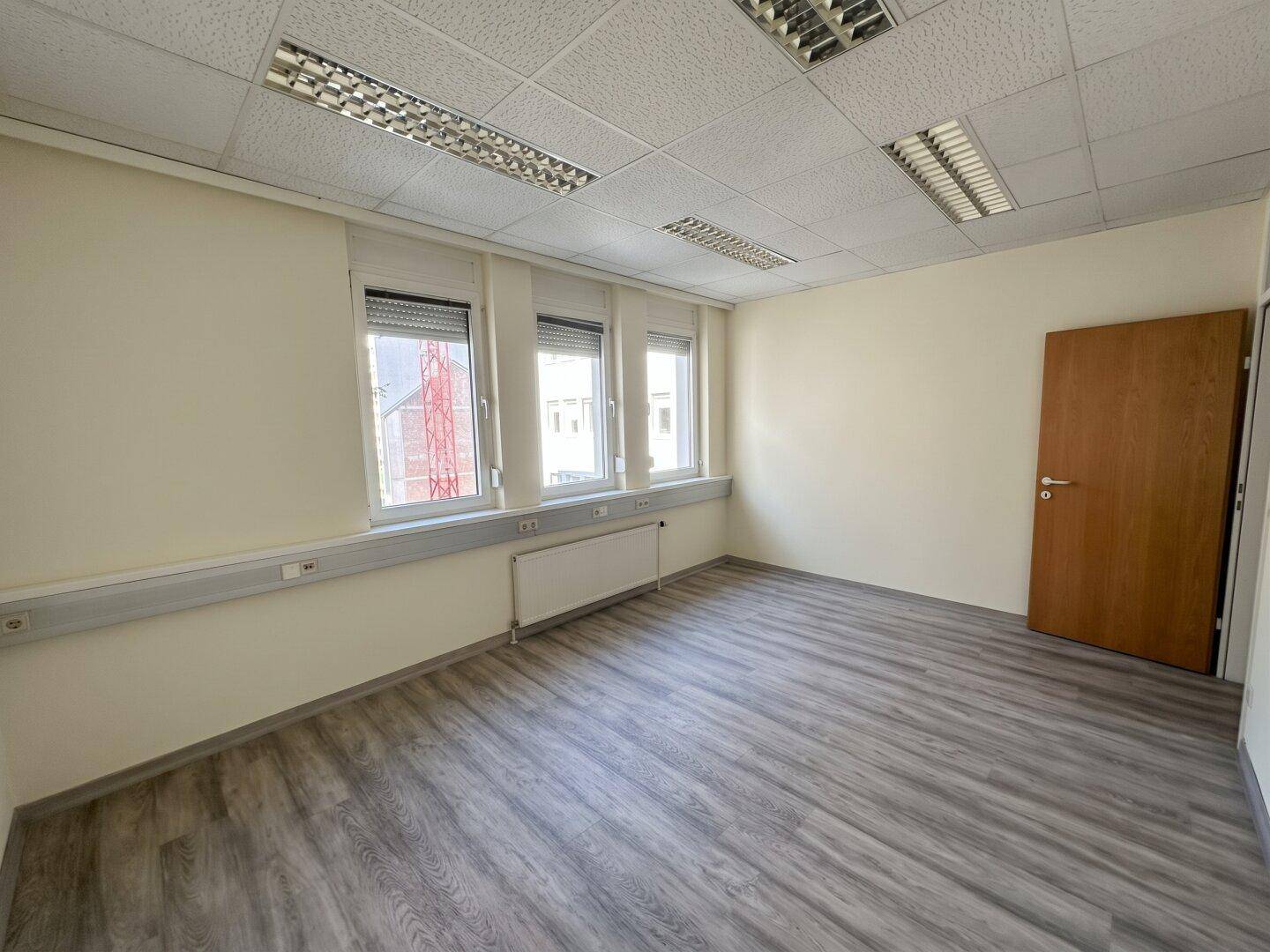 Leeres Büro mit Laminatboden und Fenstern mit Rollläden, bereit für individuelle Gestaltung.