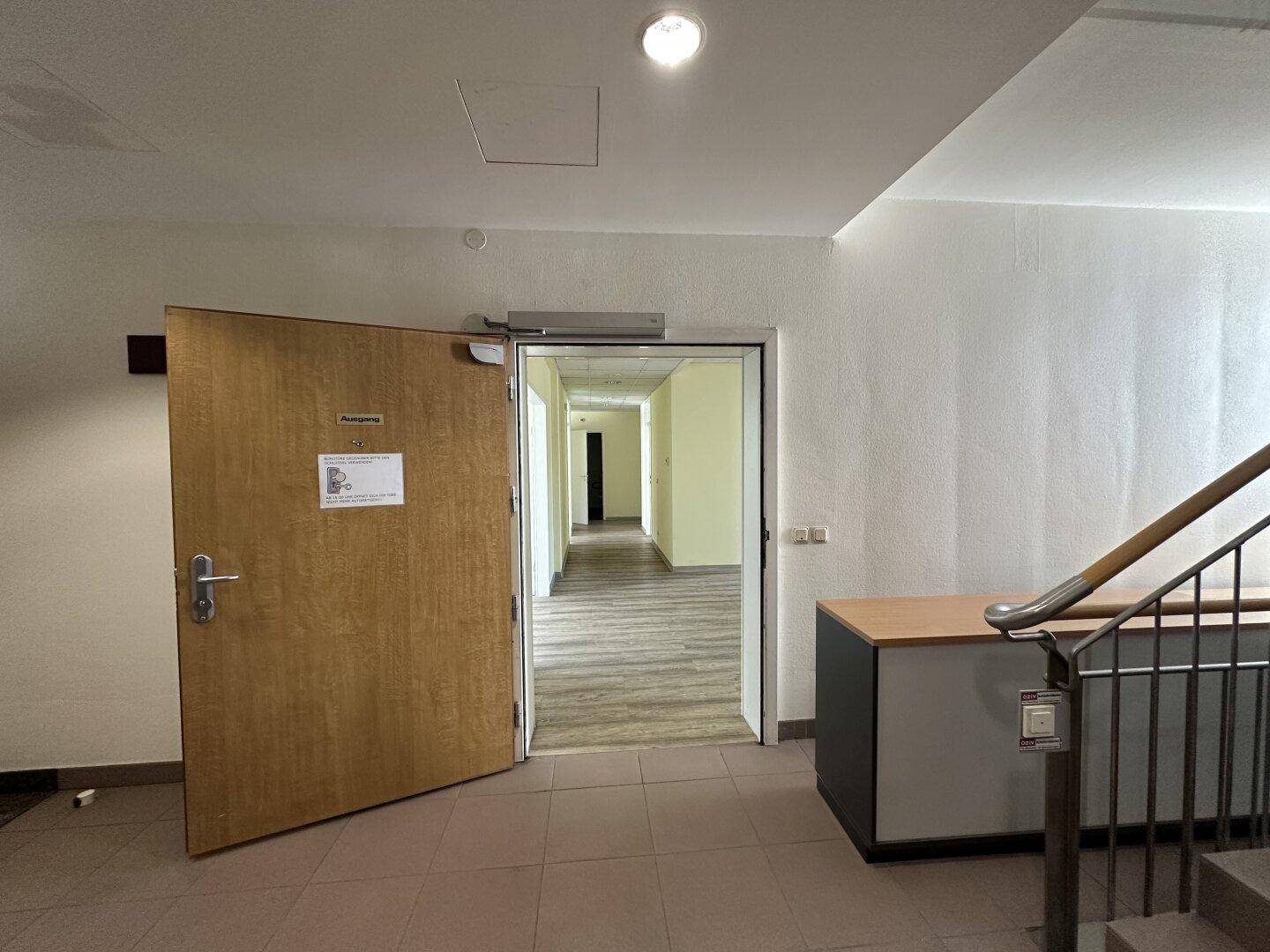 Eingangsbereich mit offener Holztür, die zu einem langen Flur führt, und einer Treppe im Vordergrund.