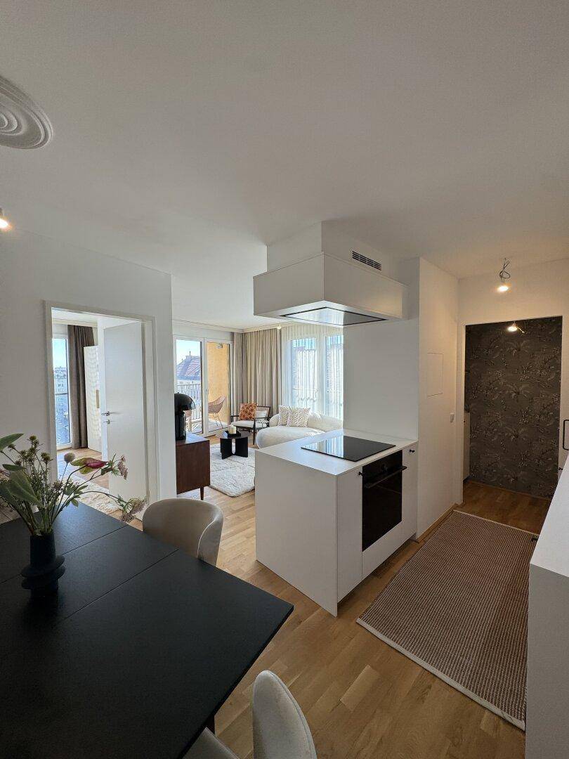 Offener Wohn- und Essbereich mit moderner Kücheninsel und Zugang zum Balkon.