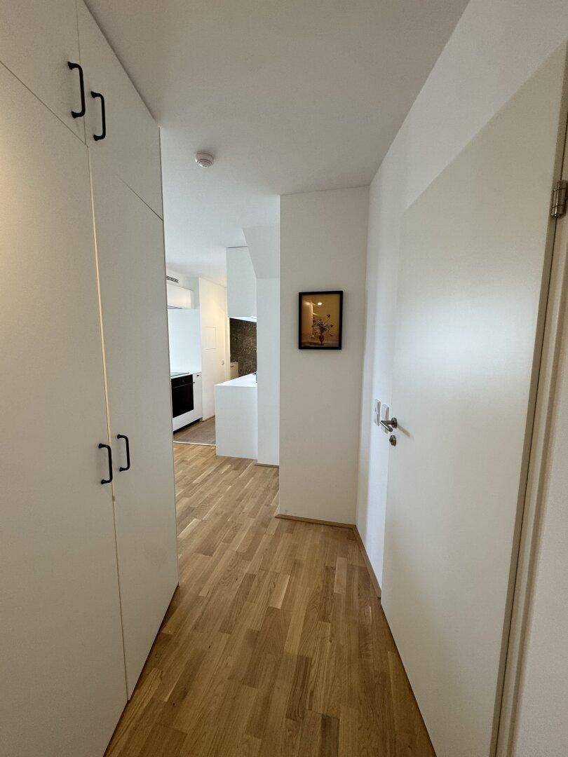 Heller Flur mit Einbauschränken und Holzboden, führt in den Wohnbereich.