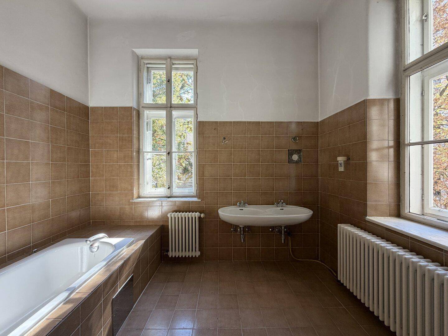 Geräumiges Badezimmer mit Badewanne, Doppelwaschbecken und zwei Fenstern.