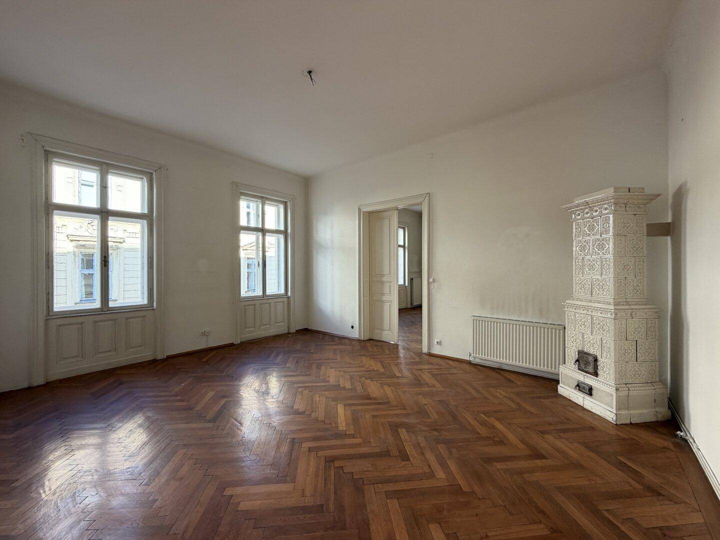 Geräumiges Wohnzimmer mit elegantem weißem Kachelofen und klassischem Fischgrätparkett.