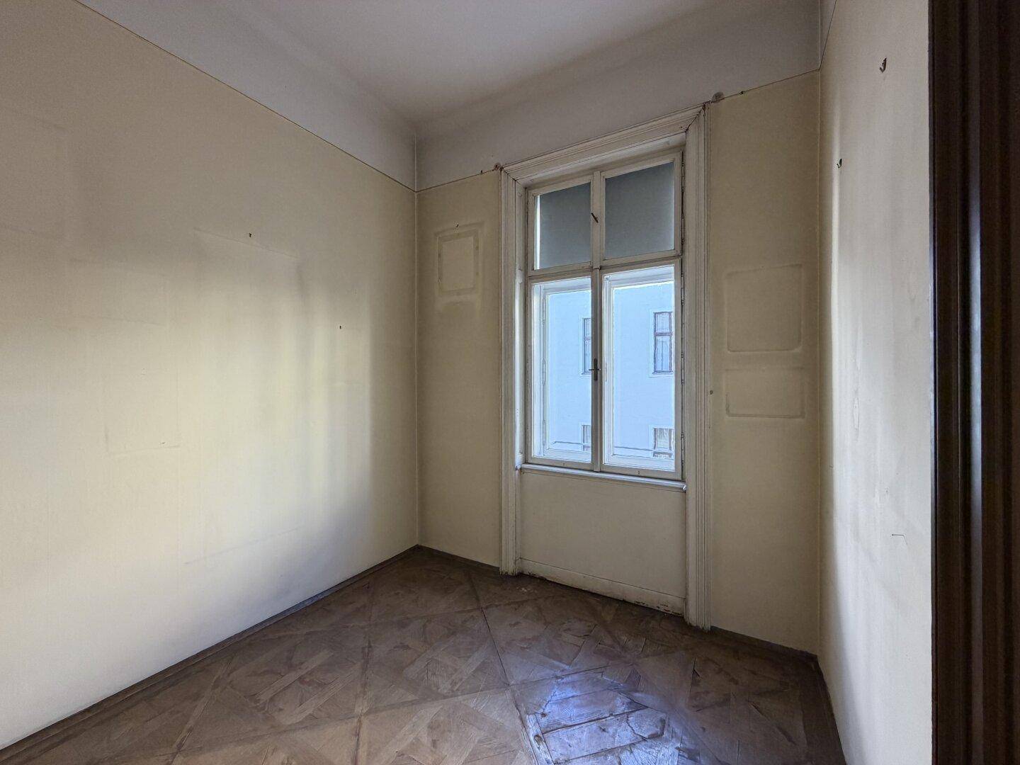 Leerer Raum mit Fenster und Parkettboden, bereit für eine individuelle Gestaltung.