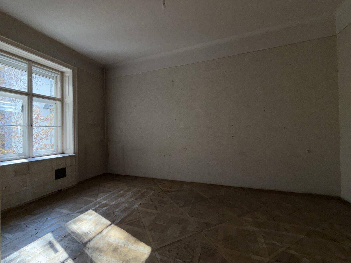 Heller Raum mit Parkettboden und einem großen Fenster, das den Raum mit Licht füllt.