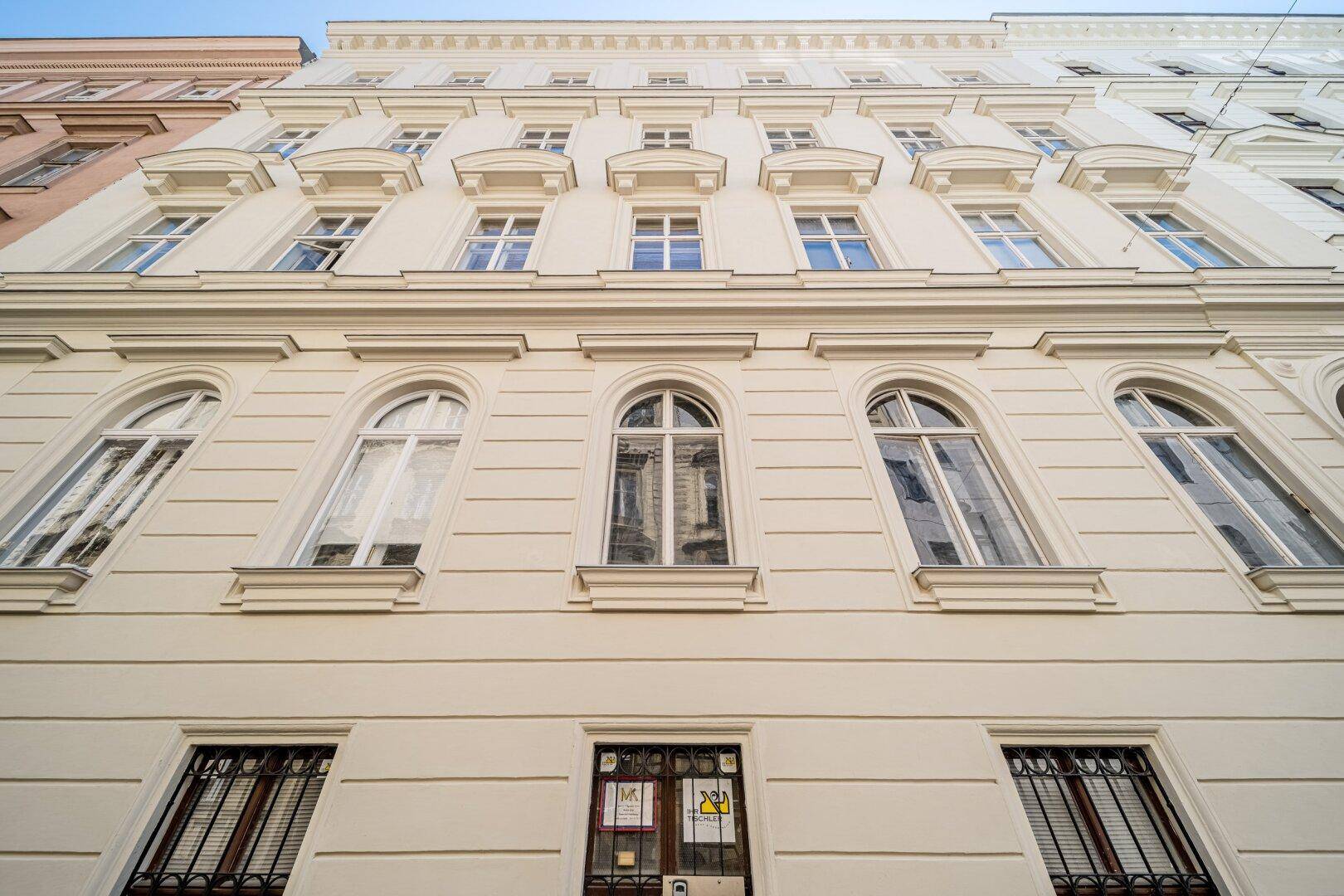 Beeindruckende Altbaufassade mit hohen Fenstern und architektonischen Details unter blauem Himmel.