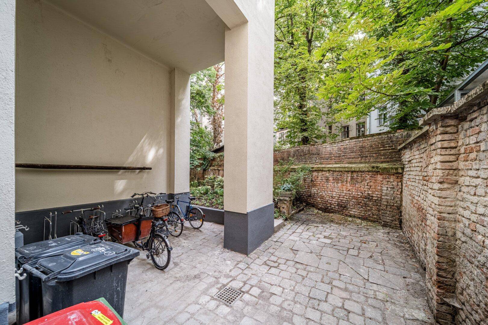 Gepflasterter Innenhof mit Fahrradabstellplatz und einer alten Ziegelmauer.