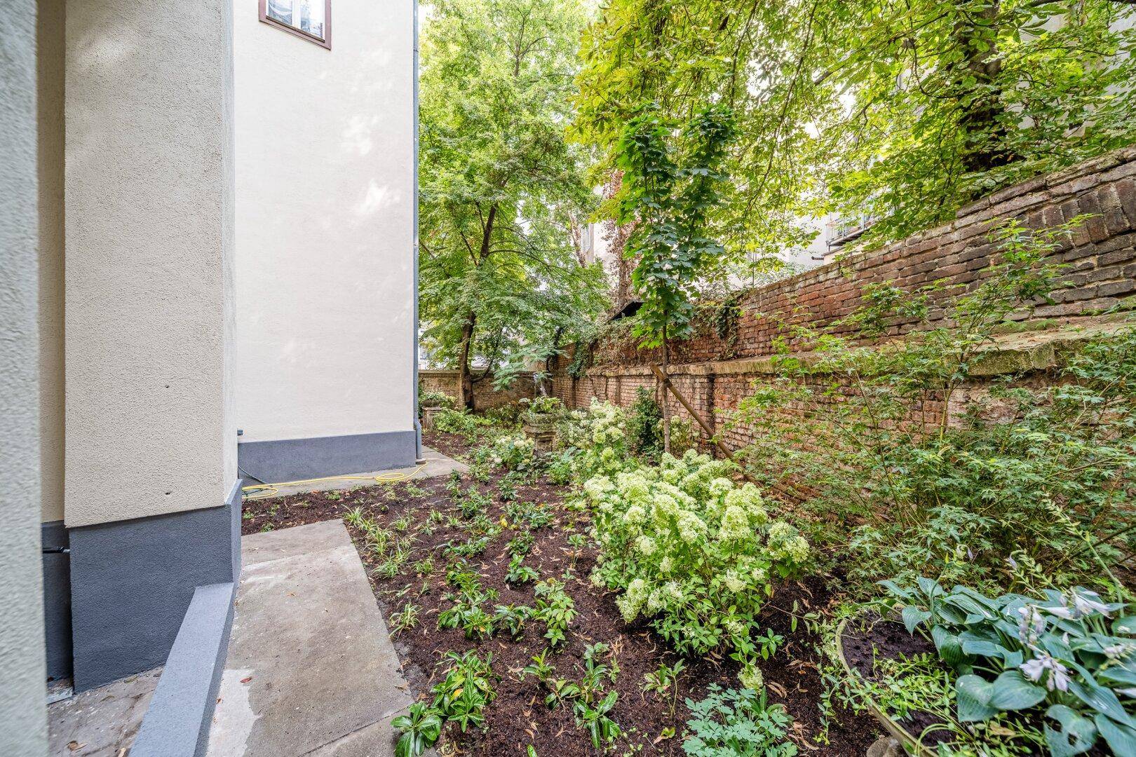 Kleiner, gepflegter Gartenbereich mit jungen Pflanzen und einer historischen Ziegelmauer.