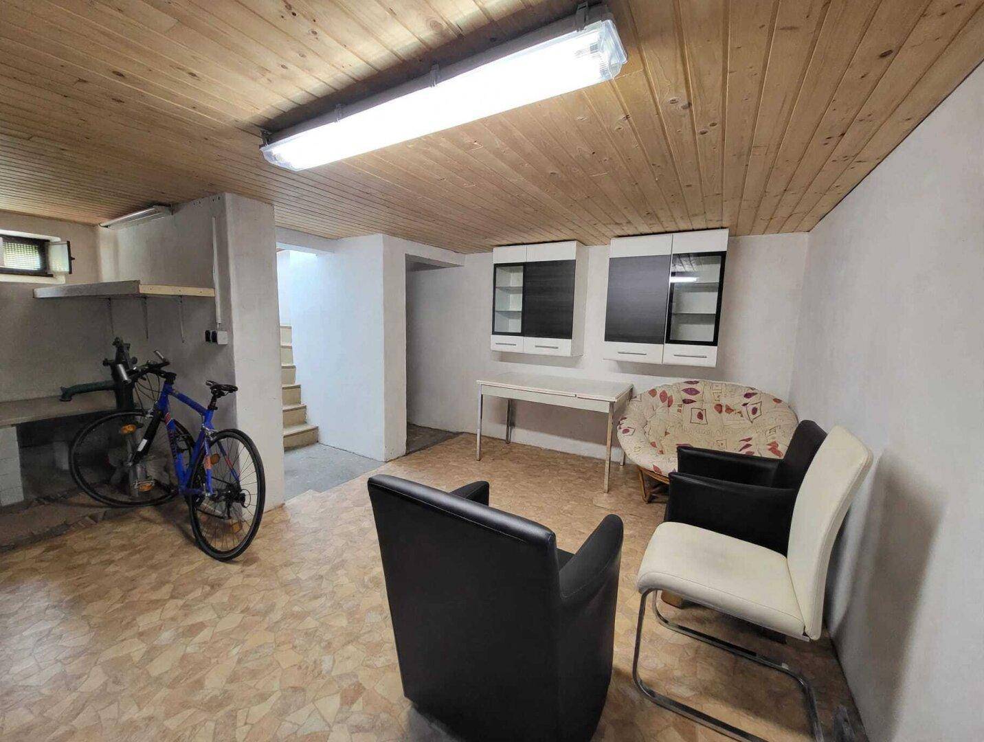Geräumiger Kellerraum mit Holzdeckenverkleidung, Sitzgelegenheiten und Fahrradabstellplatz.