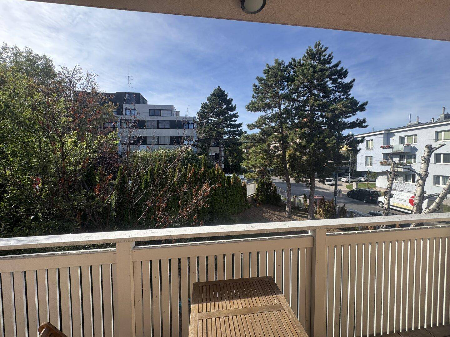Sonniger Balkon mit Holztisch und Blick auf die umliegende Wohngegend.