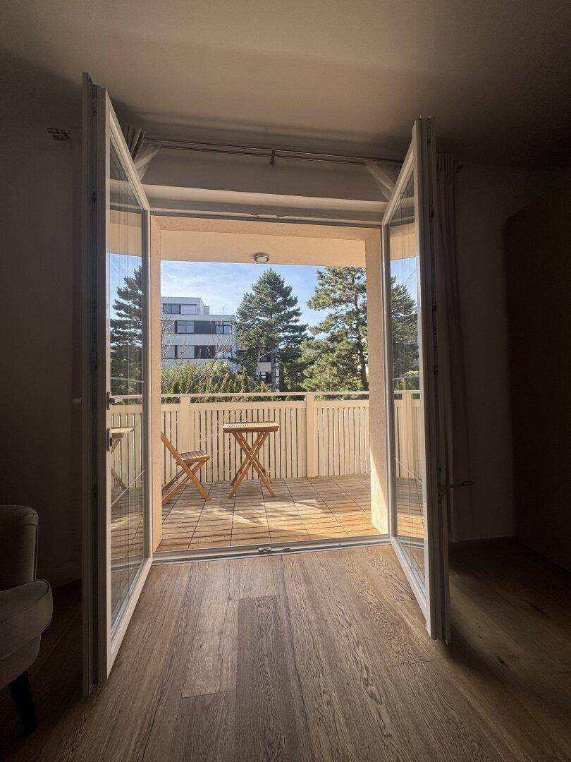 Heller Raum mit Holzboden und weit geöffneten Türen zum Balkon.