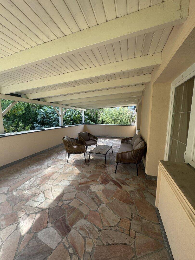 Überdachte Terrasse mit bequemen Outdoor-Möbeln und Steinplattenboden, ideal zum Entspannen.