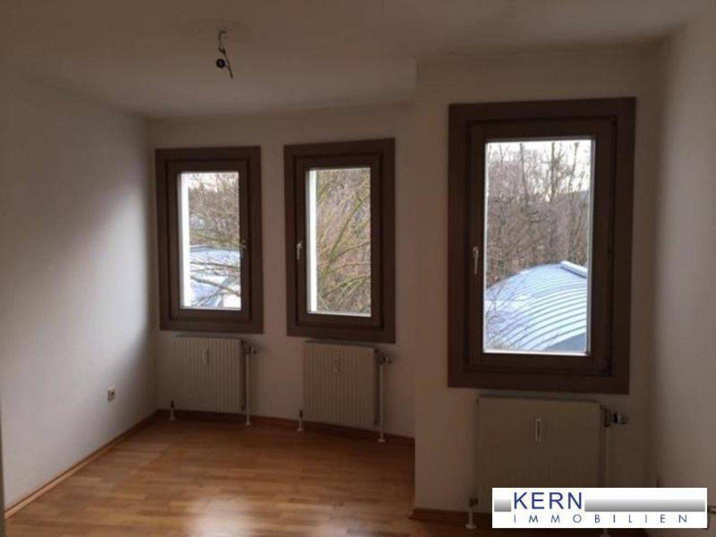Helles Zimmer mit drei Fenstern, Holzboden und Heizkörpern, bietet eine angenehme Atmosphäre.