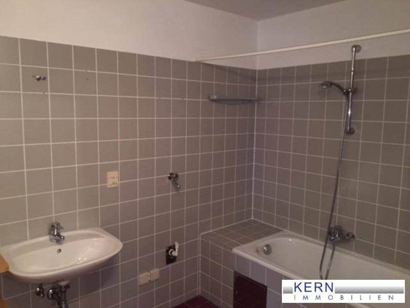 Gefliestes Badezimmer mit Badewanne, Waschbecken und Duschvorrichtung, in gutem Zustand.