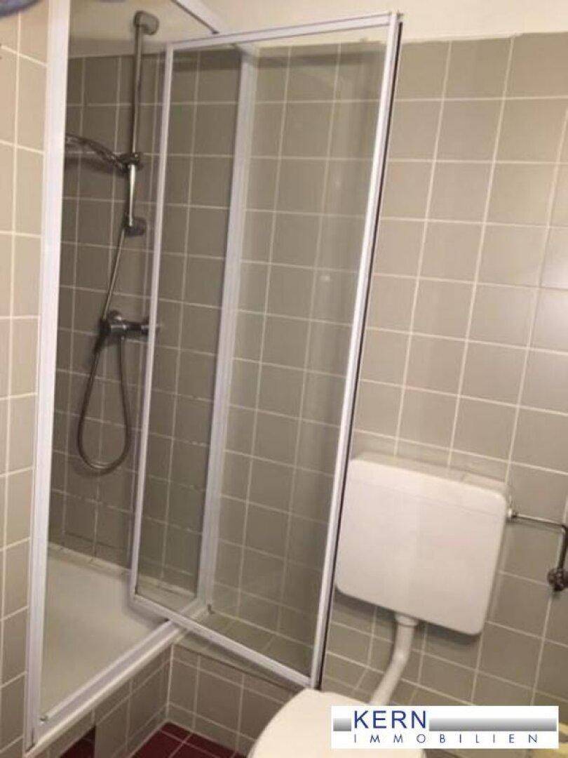 Badezimmer mit Duschkabine und Toilette, ausgestattet mit grauen Wandfliesen und roten Bodenfliesen.