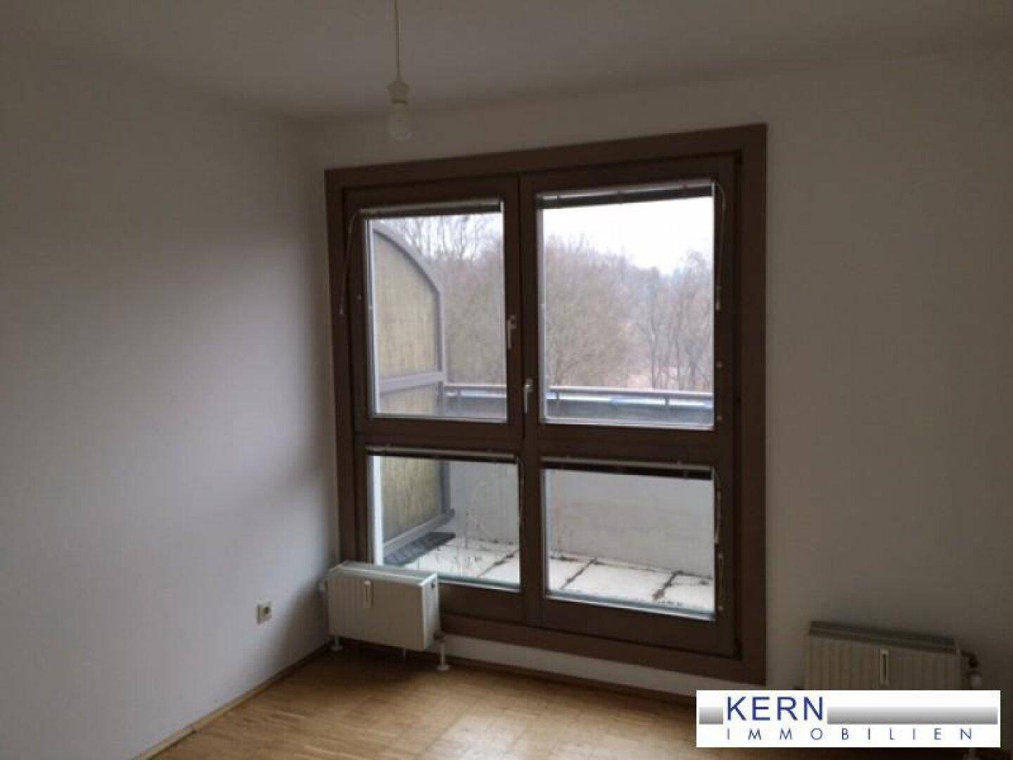 Helles Zimmer mit großem Fenster und Holzfußboden, bietet einen Ausblick ins Grüne.